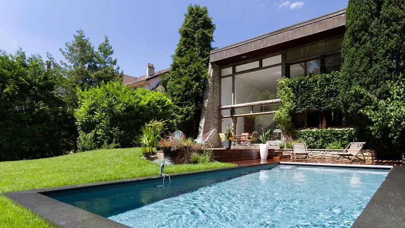 Bassin de nage à l'eau sombre devant une maison à grandes baies et bardage bois, pelouse et terrasse de bois, jardin boisé dense, transats — jardin et bassin Aqua System, ouest parisien
