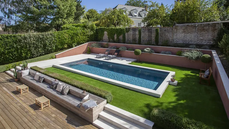 Bassin bordé de margelles claires, arbre planté au bord, terrasse en bois et haies dans une propriété de l'ouest parisien